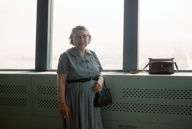 A happy visitor to the observation deck in 1962, cigarette in hand.  Photographer's handbag on ledge.